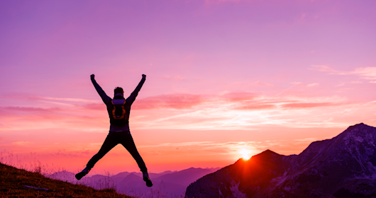 Man on a hike in the mountains jumping at sunset